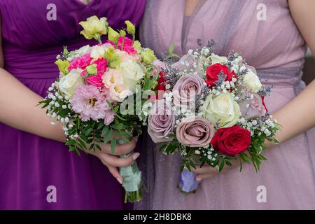 Brautjungfern oder nahestehenden weiblichen Gästen, die schöne Tüllkleider in Lavendel und Flieder tragen und elegante gemischte Blumensträuße halten, Nahaufnahme der Frauen Stockfoto