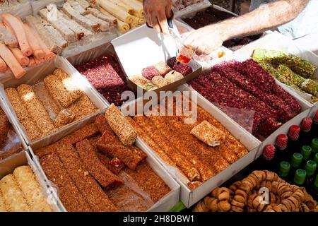 Verschiedene türkische Köstlichkeiten oder Lokum-Süßigkeiten auf dem türkischen Basar-Markt. Händler, der Box mit Lokumrollen für Touristen macht. Stockfoto