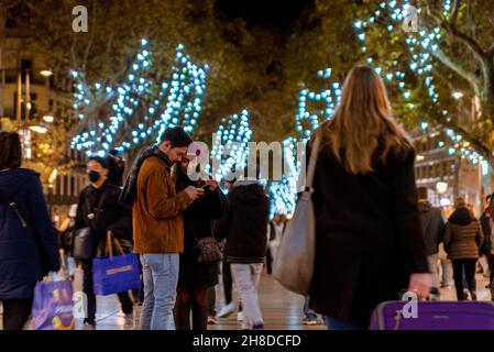 Ein junges Touristen-Paar schaut auf das Telefon, während es nachts unter den Weihnachtslichtern in der Stadt in der Hauptstraße Las Rambl Fotos macht Stockfoto