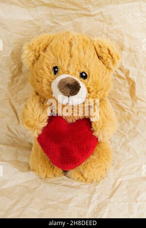 Eine Teddybärpuppe, die ein herzförmiges Kissen mit Liebe hält Stockfoto
