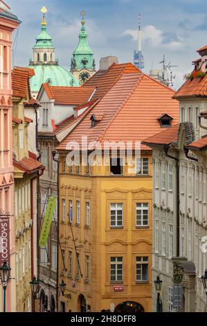 Farbenfrohe Gebäude säumen die malerische Nerudova-Straße in der Prager Malá Strana mit der Kuppel und dem Glockenturm der Nikolaikirche am Himmel Stockfoto