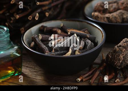 Schwarze Schale mit gemeinsamen Beinwell- oder symphytum officinale-Wurzeln. Flasche Infusion oder Tinktur. Getrocknete comfrey officinalis Wurzeln, Knitbone und Bistort, SNA Stockfoto