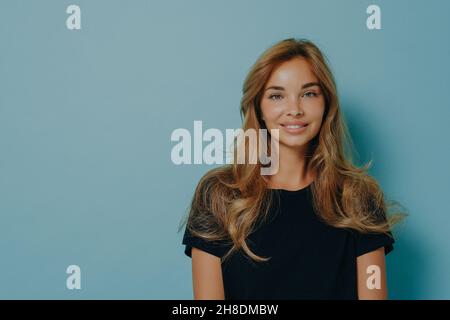 Langhaarige Frau blickt direkt auf die Kamera mit zärttem Ausdruck, gekleidet in legeres schwarzes T-Shirt Stockfoto