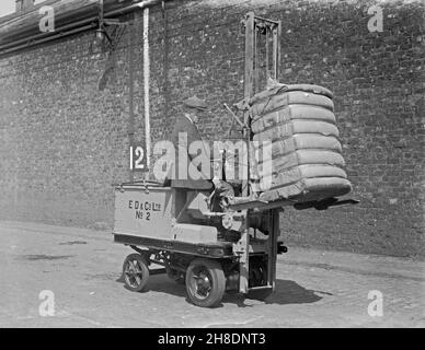 Früher batteriebetriebener Transport – Hier wird bei E D and Co Ltd, einem Schiffs- und Lagerunternehmen in Liverpool Docks, Lancashire, England, in den frühen Jahren des 20. Jahrhunderts, ein Gabelstapler zum Transport eines schweren Ballens verwendet. In den frühen Jahren des Kraftverkehrs waren elektrisch betriebene Fahrzeuge eine gute Option im Vergleich zu benzinbetriebenen Fahrzeugen für den Kurzstrecken-gewerblichen Verkehr, wie etwa den Transport von Waren in Fabriken. Dies ist einem alten Original-Glas-Negativ entnommen – einem Vintage-Foto aus dem 20th. Jahrhundert. Stockfoto