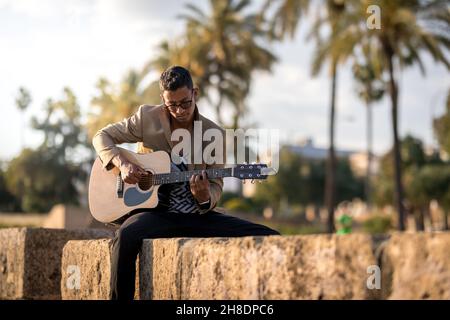 Lateinischer Mann spielt Gitarre auf der Straße während des Sonnenuntergangs in Panorama Stockfoto