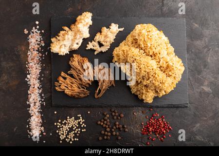 Rohe Sparassis (Blumenkohlpilz), Hericium, Clavaria (Korallenpilz) auf schwarzem Betongrund mit Salz und Gewürzen. Draufsicht, flach liegend. Stockfoto