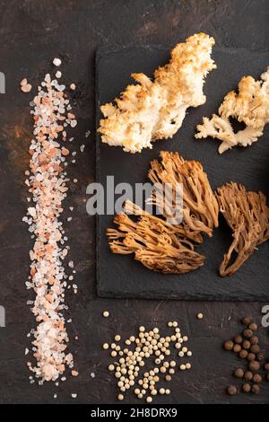 Rohe Sparassis (Blumenkohlpilz), Hericium, Clavaria (Korallenpilz) auf schwarzem Betongrund mit Salz und Gewürzen. Draufsicht, flach liegend. Stockfoto