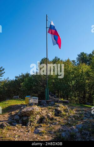 Slowenische Flagge auf dem Gipfel des Skabrijel in der Nähe von Nova Gorica in der Region Primorska im Westen Sloweniens. An der Basis befindet sich eine Kiste mit dem Gipfelregister Stockfoto