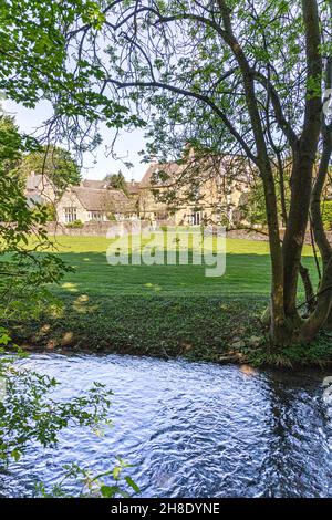 Das Herrenhaus neben dem kleinen Fluss Windrush, der durch das Cotswold-Dorf Naunton, Gloucestershire, Großbritannien, fließt Stockfoto