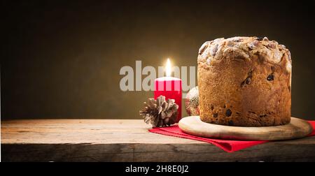 Sehr einfache Weihnachten, ein Panettone und eine brennende rote Kerze. Weihnachtliche Atmosphäre. Platz für Text. Stockfoto