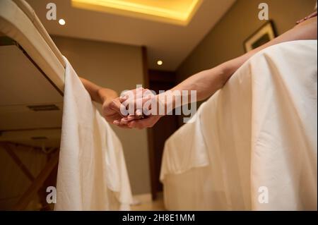 Konzentrieren Sie sich auf die Hände eines liebevollen Paares, liegen Sie auf dem Massageliegen und halten Sie sich bei der Körperpflege im Wellness-Center Hand in Hand. Zuneigung, zehn Stockfoto