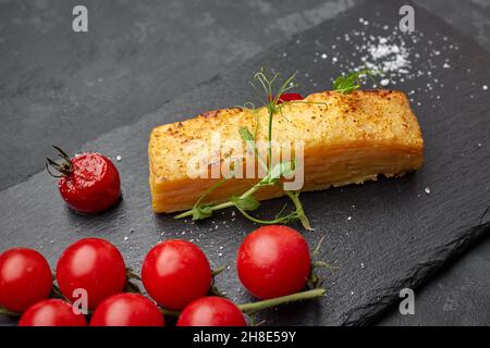 Dauphinua Kartoffelgratin mit Kirschtomaten auf schwarzem Stein Stockfoto