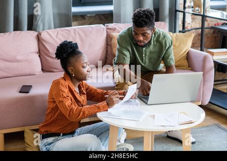 Seriöses junges afroamerikanisches Paar, das mit Papieren und Laptop am Couchtisch sitzt und über Finanzen diskutiert Stockfoto