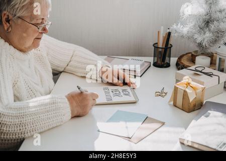 Gesunde Neujahrvorsätze für ältere Erwachsene. Ältere ältere alte Frau in weißem Pullover schriftlich handgeschriebenen Text Neujahr Auflösungen in offener Stockfoto