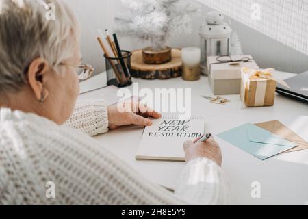 Gesunde Neujahrvorsätze für ältere Erwachsene. Ältere ältere alte Frau in weißem Pullover schriftlich handgeschriebenen Text Neujahr Auflösungen in offener Stockfoto