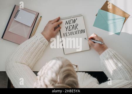 Gesunde Neujahrvorsätze für ältere Erwachsene. Ältere ältere alte Frau in weißem Pullover schriftlich handgeschriebenen Text Neujahr Auflösungen in offener Stockfoto