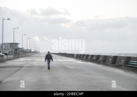 Zu Fuß, entlang, Promenade, kämpfen, zu, bleiben, aufrecht, und, nicht, werden, geblasen, über,. Liverpool, Großbritannien. 26th. November 2021. Foto aus New Brighton von Windböen, die mit rauer See wehen.Leuchtturm in New Brighton und Liverpool im Hintergrund. Stockfoto