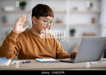 Lächelnder koreanischer molliger Junge winkt am Laptop-Bildschirm Stockfoto