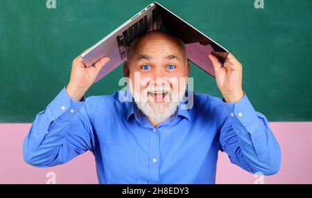 Glücklicher bärtiger Mann mit Laptop über dem Kopf. Lächelnder Lehrer mit Notizbuch im Klassenzimmer Stockfoto