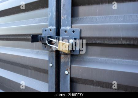 Abgewinkelte Ansicht eines gelben Vorhängeschlosses, mit dem zwei große Metalltüren in einem Lagerraum im Freien verschlossen bleiben Stockfoto