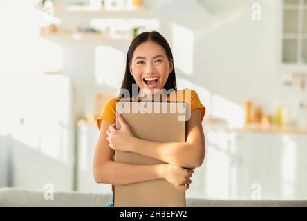 Zufrieden mit dem Kauf. Porträt der aufgeregt asiatische Frau umarmt Karton Karton Karton, erhielt Paket, zufrieden mit Geschenk Stockfoto
