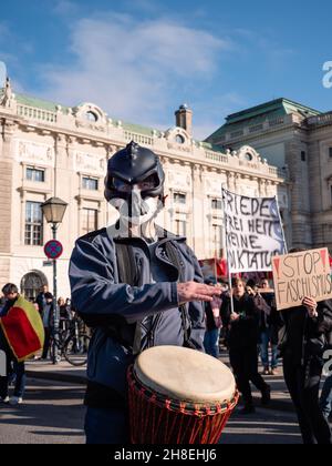 Wien, Österreich - November 20 2021: Maskierter Anti-Vax Covid-19 Demonstrator Trommeln auf dem Heldenplatz, trägt ein Stockfoto