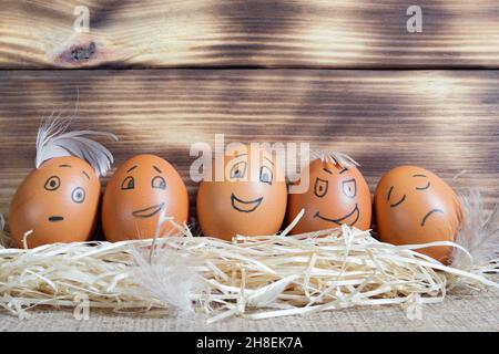 Fünf braune Eier mit lustigen Gesichtern auf Holzhintergrund Stockfoto