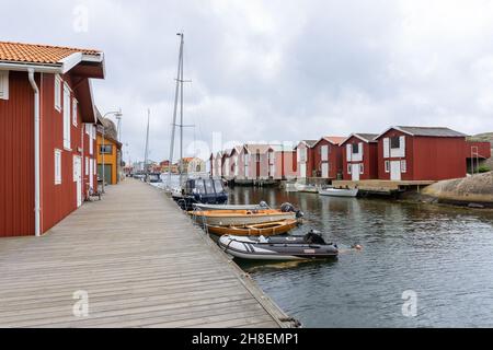 Smögen, Schweden - 9. Juni 2021: Spaziergang über eine Holzbrücke entlang des wasserhanels mit Segelbooten und Fischerhütten auf beiden Seiten des Kanals Stockfoto
