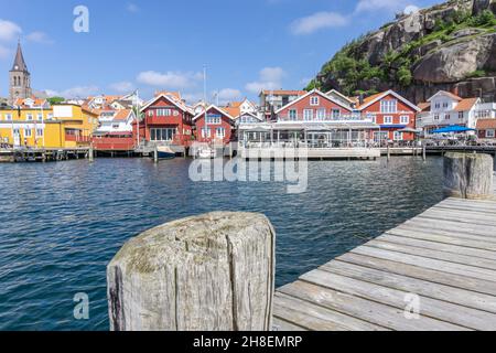 Fjällbacka, Schweden -9. Juni 2021: Blick auf den Strand in einer Touristenstadt mit Pier im Vordergrund und typisch schwedischen Gebäuden im Hintergrund Stockfoto