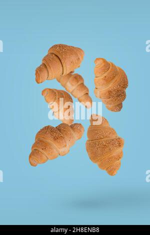 Frisch gebackene Croissants fliegen isoliert auf hellblauem Hintergrund in der Luft. Kreatives Frühstückskonzept. Stockfoto