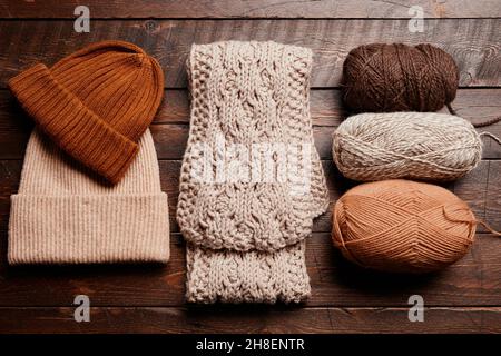 Draufsicht auf Strickschal und Hut mit Wolle auf dunklem Holzhintergrund, Stricken und Hobby, Kopierraum Stockfoto