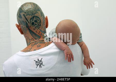 Vater mit Tattoos hält seinen neugeborenen Sohn fest Stockfoto