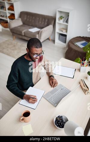 Hochwinkelporträt eines jungen afroamerikanischen Mannes, der eine Brille trägt, während er von zu Hause aus arbeitet und einen Laptop benutzt Stockfoto