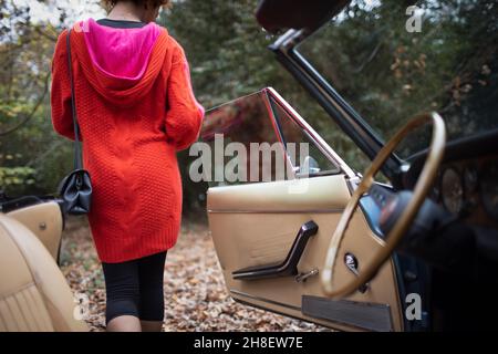 Junge Frau, die im Herbstpark aus dem Cabrio aussteigen wird Stockfoto