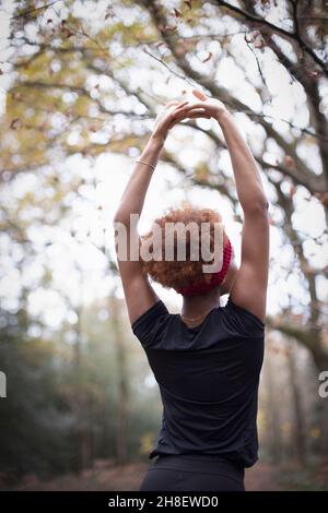 Junge Joggerin, die im Herbstpark die Arme streckt Stockfoto