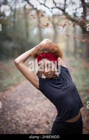 Junge Joggerin, die im Herbstpark die Arme streckt Stockfoto