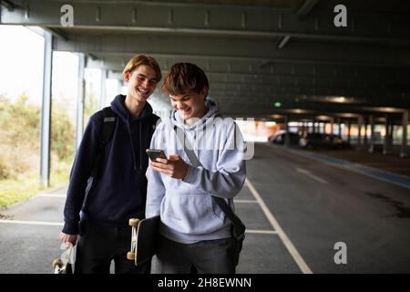 Teenager mit Smartphone und Skateboards auf dem Parkplatz Stockfoto