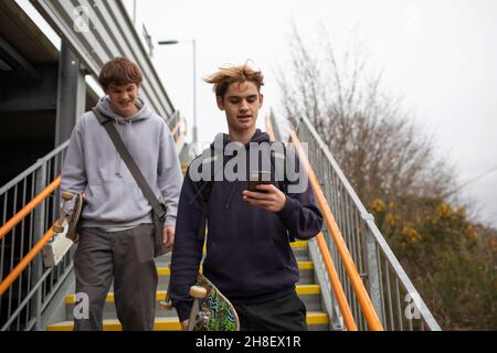 Teenage-Jungs mit Skateboards und Smartphone, die Treppen hinuntersteigen Stockfoto