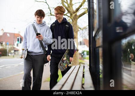 Teenagerjungen mit Skateboards und Smartphone an der Bushaltestelle Stockfoto