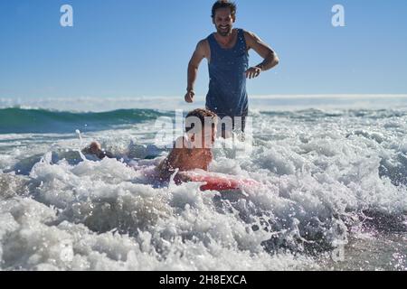 Glücklicher Vater und Sohn boarden in sonniger Meeresbrandung Stockfoto