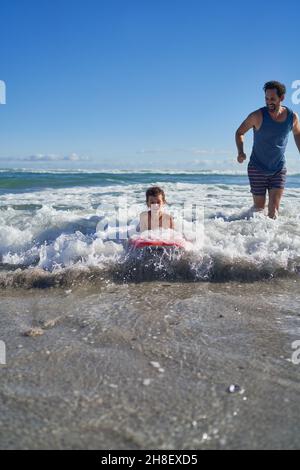 Vater und Sohn boarden in sonniger Meeresbrandung Stockfoto