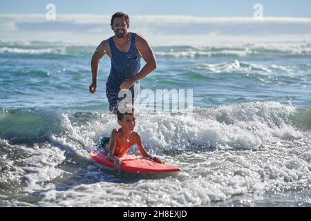 Glücklicher Vater und Sohn boarden in sonniger Meeresbrandung Stockfoto