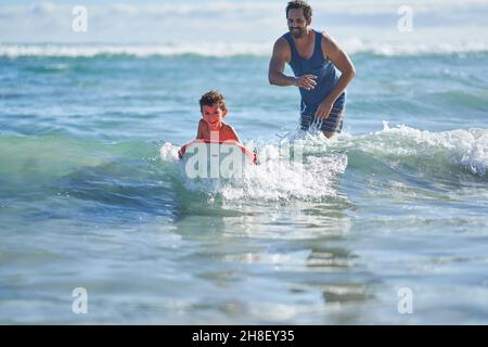 Glücklicher Vater und Sohn boarden in sonnigem Ozean Stockfoto