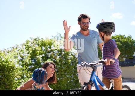 Glücklicher Vater und Sohn auf dem Fahrrad High Fiving in sonniger Auffahrt Stockfoto