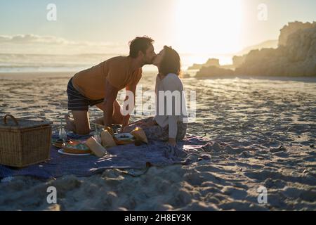 Zärtliches Paar küsst sich auf einer Picknickdecke am sonnigen Sommerstrand Stockfoto