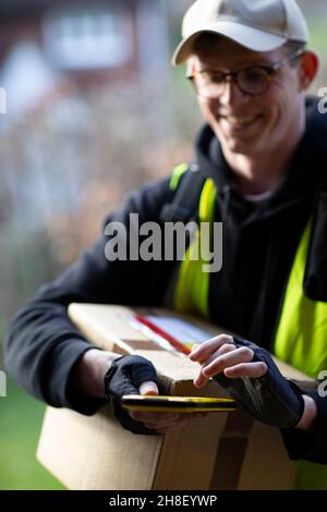 Lächelnder männlicher Kurier mit Smartphone, der das Paket liefert Stockfoto