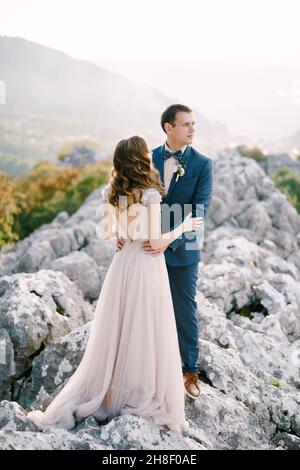Der Bräutigam umarmt die Braut an der Taille auf einem felsigen Berg Stockfoto