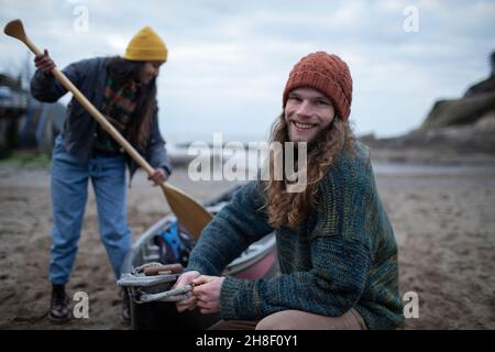 Portrait sorgloses junges Paar, das Kanu am Strand vorbereitet Stockfoto