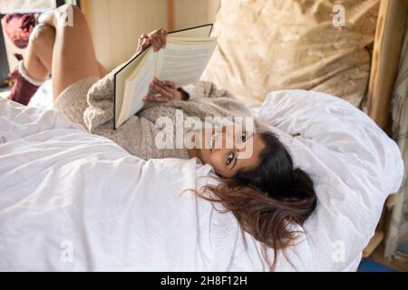 Portrait glückliche junge Frau entspannt mit Buch im Bett Stockfoto