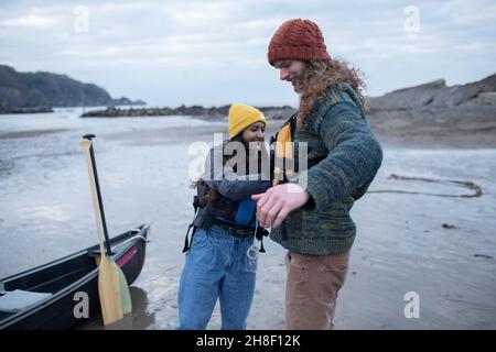 Junges Paar, das sich auf Kanufahrten am Meeresstrand vorbereitet Stockfoto